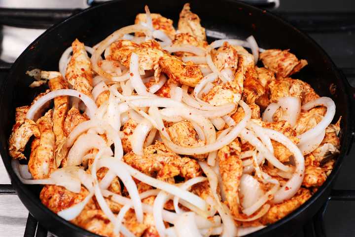 Cocinar fajitas de pollo en una sartén con cebollas en rodajas.